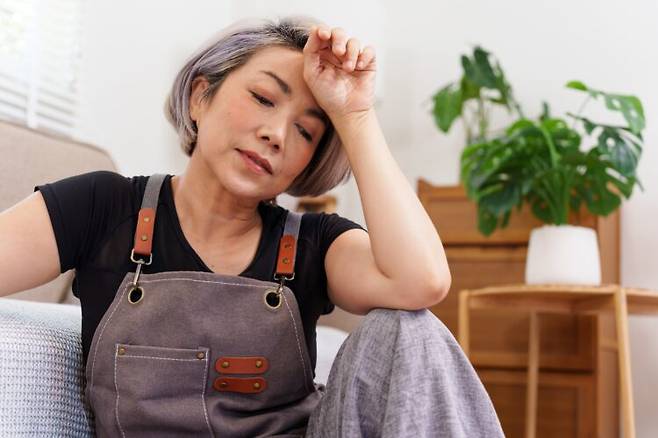 에이프런을 두른 중년 여성이 거실에 앉아 쉬고 있다. 만성피로증후군(ME/CFS)은 충분히 쉬어도 회복되지 않는 탈진과 브레인포그를 특징으로 하는 병으로 알려져 있다. 사진=게티이미지뱅크