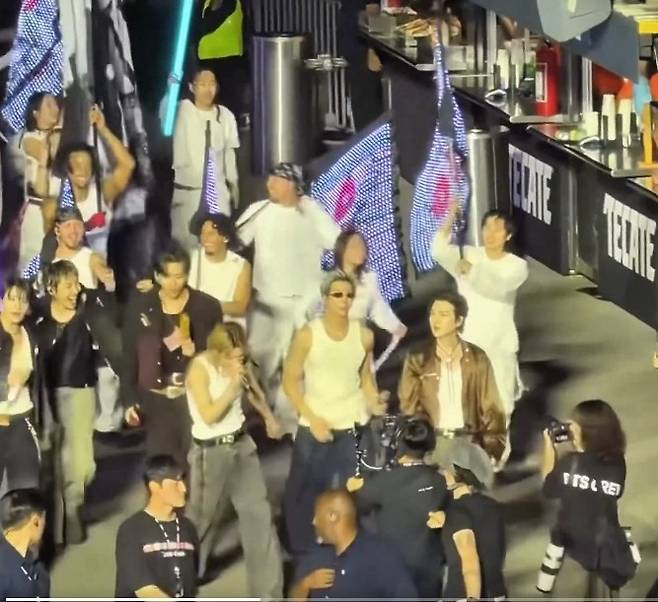 퍼레이드 도중 노점에서 반데리야를 사들고 온 뷔를 보고 제이홉이 웃는 모습 사진 엑스 (트위터) 팬 계정
