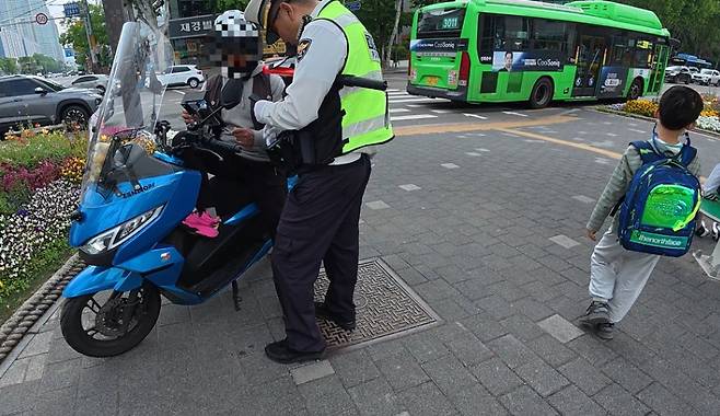 지난 12일 오후 2시 50분께 서울 강남구 대치역 사거리에서 경찰이 보행자보호의무를 위반한 배달 기사에게 범칙금을 부과하는 가운데 옆으로 초등학생이 지나가고 있다. 이날 서울경찰청은 서울 49곳의 스쿨존에서 ‘하굣길 교통 법규 위반 단속’을 실시했다. 이영기 기자.