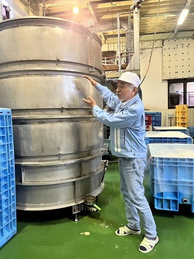 작업복 차림으로 발효 탱크 앞에서 양조 과정을 설명하는 노리츠구 사장