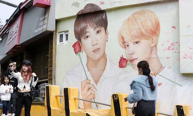 부산 감천문화마을에서 외국인 관광객이 BTS 멤버 벽화를 배경으로 사진을 찍고 있다. [뉴스1]