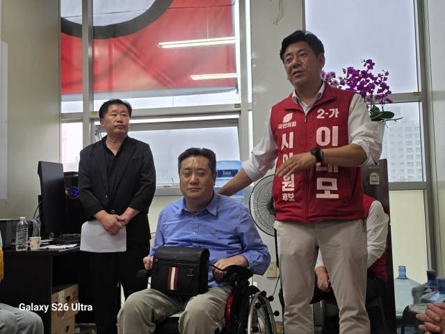 ▲국민의힘 이태모 논산시의원 후보(오른쪽)가 개소식에서 휠체어를 타고 참석한 친형 이태규 다사랑연합의원 원장을 소개하며 인사말을 하고 있다. 이날 행사장에서는 형제를 향한 참석자들의 응원과 박수가 이어지며 잔잔한 감동을 전했다. 사진=김흥준 기자
