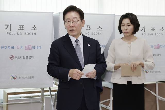 이재명 대통령이 제9회 전국동시지방선거 사전투표 첫날인 지난 5월 29일 서울 종로구 삼청동 주민센터에서 기표소에 들어가 사전투표하던 중 나와, 기표 도장이 ‘절반 정도만 찍혔는데 괜찮냐’는 취지로 선거사무원을 불러 관련 문의를 하고 있다. 오른쪽은 이 대통령 부인 김혜경 여사. [청와대통신사진기자단·연합뉴스]