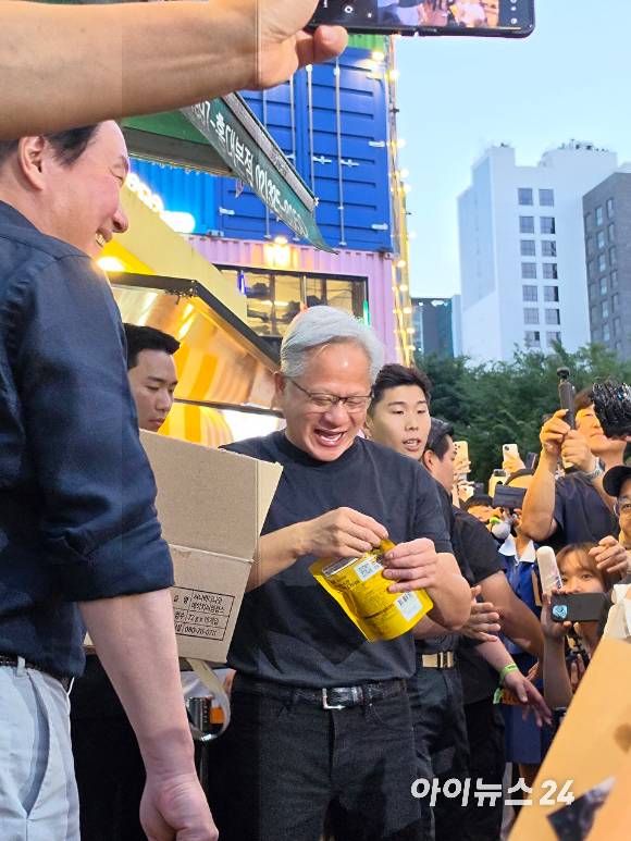젠슨 황 엔비디아 최고경영자(CEO)가 5일 서울 마포구 홍대 삼겹살집 '형님저요' 앞에서 SK하이닉스 HBM(고대역폭메모리) 과자칩을 들고 환하게 웃고 있다. 왼쪽은 최태원 SK그룹 회장. [사진=황세웅 기자]