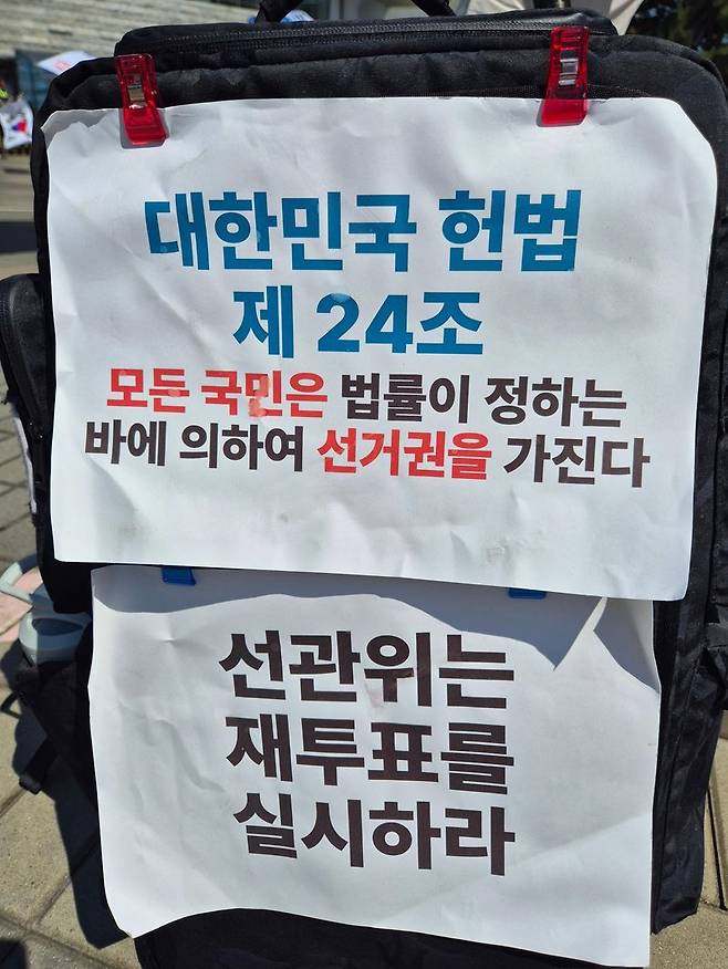 선관위에 재투표를 촉구하는 문구가 유권자의 가방에 붙어 있다. 사진=김예지 기자