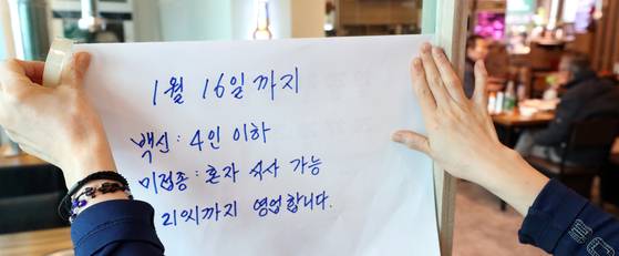 코로나19 대유행 시기인 2021년 12월 31일 서울 종로구 한 식당에서 종업원이 거리두기 연장관련 문구를 붙이고 있다. 이날 정부는 사적모임 인원을 최대 4명까지 허용하고 식당·카페 등은 오후 9시까지로 영업시간을 제한하는 거리두기 조치를 2주간 연장한다고 발표했다. 뉴스1