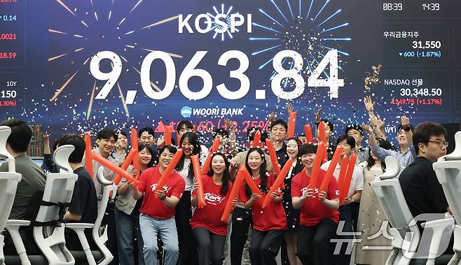 코스피 지수가 전인미답의 9000선 고지를 돌파한 18일 오후 서울 중구 우리은행 본점 딜링룸에서 직원들이 코스피 종가를 배경으로 축하 세리머니를 하고 있다. 2026.6.18 ⓒ 뉴스1 오대일 기자