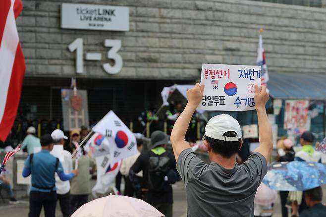 6·3 지방선거 투표용지 부족 사태로 인한 '개표소 봉쇄 시위'가 이어지고 있는 지난 18일 서울 송파구 올림픽공원 핸드볼경기장 출입문 앞에서 참가자들이 구호를 외치고 있다. ⓒ연합뉴스