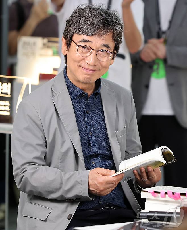 유시민 작가가 25일 서울 강남구 코엑스에서 열린 서울국제도서전 '돌베개·평산책방' 부스에서 문재인 전 대통령, 탁현민 전 청와대 의전비서관과 북토크 중 책을 읽고 있다. 2026.6.25 ⓒ 뉴스1 김진환 기자