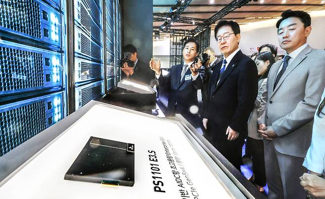 이재명 대통령이 30일 광주광역시 김대중컨벤션센터에서 열린 서남권 첨단산업 발전 비전 국민보고회에 앞서 강훈식 대통령 비서실장(오른쪽)과 함께 곽노정 SK하이닉스 사장(왼쪽)으로부터 인공지능(AI) 데이터센터에 사용되는 초고용량 솔리드스테이트드라이브(SSD) 제품인 PS1101에 관한 설명을 듣고 있다. 이날 삼성·SK 등은 서남권에 총 896조원 규모의 투자계획을 밝혔다. [청와대 사진기자단]