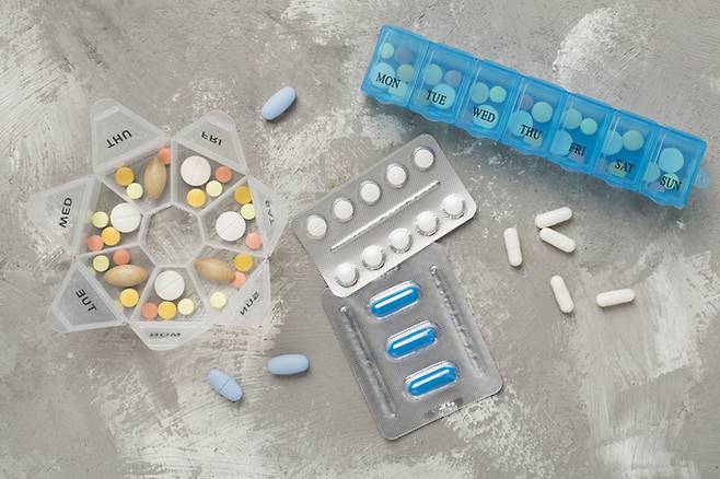Daily pill organizer with medications on concrete background, top view
