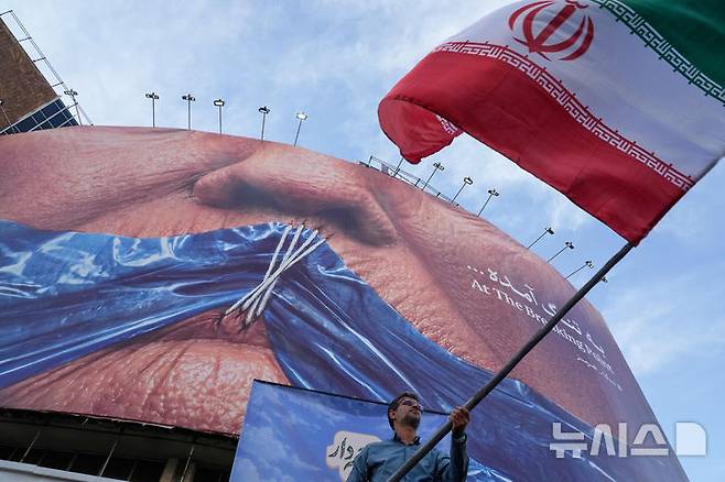 [테헤란=AP/뉴시스] 16일(현지 시간) 파이낸셜타임스(FT)에 따르면 미군은 이날 이란 내륙과 남부 지역의 교량, 공항, 전력시설 등을 잇달아 타격했다. 사진은 지난 5월6일(현지시간) 이란 수도 테헤란 도심 광장에서 한 남성이 친정부 캠페인의 하나로 이란 국기를 흔들고 있다. 2026.07.17.