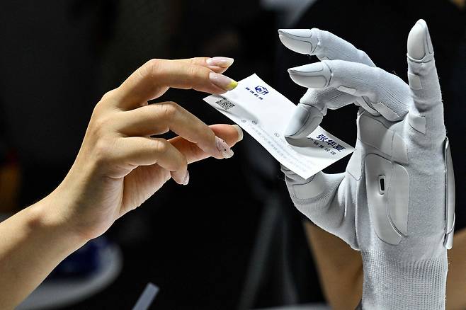 지난 18일 중국 상하이에서 열린 세계인공지능대회(WAIC)에서 한 여성이 자이노바(Xynova) 테크놀로지가 만든 로봇 손에 명함을 건네고 있다. /AFP 연합뉴스