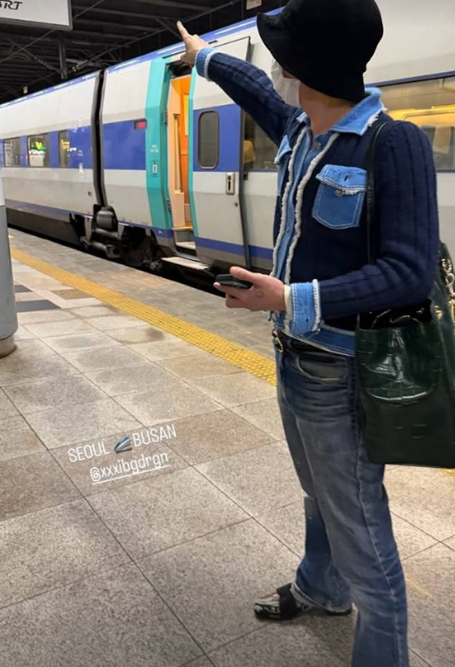 G-Dragon, a member of the group BIGBANG, is garnering attention after photos were released showing him traveling on the Korea Train Express following his schedule in Busan. On the 19th, G-Dragon attended the opening ceremony of the 48th UNESCO World Heritage Committee held at BEXCO in Busan and received his letter of appointment as a goodwill ambassador for the National Heritage Administration.On the 20th, photos of him traveling between Seoul and Busan on the Korea Train Express were posted on a social media account run by G-Dragons staff. Unlike his usual use of private cars or jets, his daily routine of using public transportation caught the attention of fans.In the released photos, G-Dragon displayed his unchanging charisma despite having his face covered by a mask. He personally took photos of the train interior and station scenery, sharing his relaxed demeanor while on the move.Meanwhile, BIGBANG, to which G-Dragon belongs, is scheduled to hold their 20th anniversary world tour, XX: COSMOS, at the Goyang Sports Complex from August 21 to 23.
