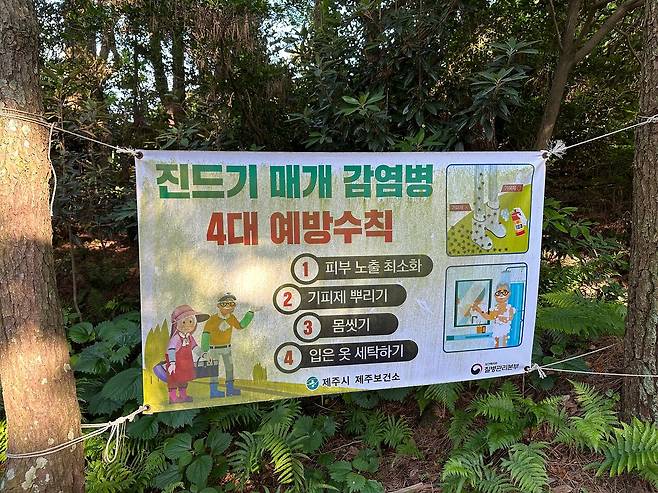 기후변화로 더위가 길어지면서 쯔쯔가무시증을 옮기는 털진드기의 활동 기간과 서식 범위가 넓어지고 있다. 사진은 제주시의 한 오름에 설치된 ‘진드기 매개 감염병 4대 예방수칙’ 현수막. 피부 노출 최소화, 기피제 뿌리기, 몸 씻기, 입은 옷 세탁하기 등의 안내 문구가 적혀 있다. [연합뉴스]