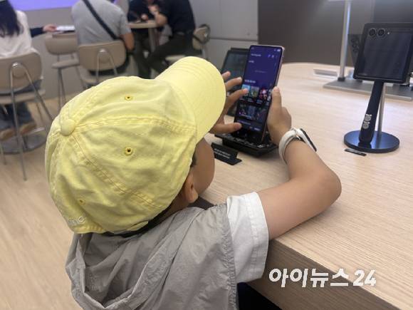 한 아이가 화면을 펼친 갤럭시 Z 플립8을 만지고 있다. 오른쪽 뒤에 있는 제품은 화면을 접은 모습.