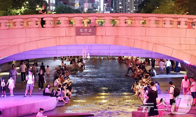 서울 전역에 폭염주의보와 열대야주의보가 동시 발효된 26일 저녁 서울 중구 청계천을 찾은 관광객과 시민들이 물가에 앉아 더위를 식히고 있다. 기상청이 지난 53년 동안의 관측 자료를 분석한 결과, 최근 10년 열대야 일수는 관측 초기보다 3배나 급증한 것으로 나타났다. 2026.7.26 ⓒ 뉴스1 오대일 기자