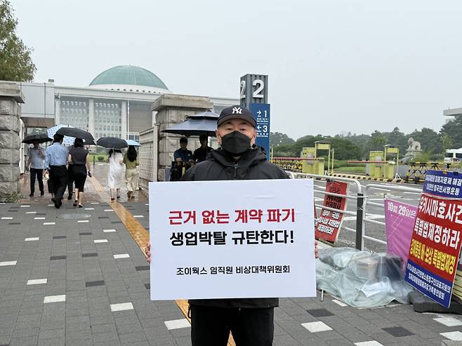 20일 서울 여의도 국회 앞에서 조이웍스 임직원 비상대책위원회 관계자가 호카 국내 총판 계약 해지에 반발하는 내용의 피켓을 들고 있다. 조이웍스 비대위 제공