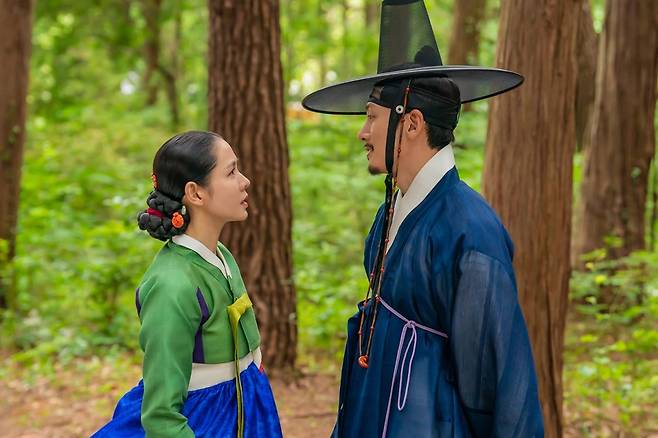 Returning after 23 years, Scandal has expanded both in scale and intensity. While the production was spectacular, the prevailing opinion is that Son Ye-jin was the only actor who managed to maintain her dignity until the end. Ji Chang-wook failed to capture the expected sensuality despite his daring exposure, and Nana, taking on her first historical drama, could not avoid controversy regarding her acting skills.The Netflix series Scandal is an eight-episode reinterpretation of the 2003 film Scandal: A Tale of Two Lovers in Joseon 23 years later. Son Ye-jin, Ji Chang-wook, and Nana play three characters entangled in desire and temptation.The visual spectacle is undeniable. From splendid hanbok and traditional houses to the meticulous portrayal of life in the Joseon Dynasty—including the processes of making paper, cultivating mulberry trees, and weaving silk—it is certainly eye-catching for viewers who appreciate the unique mise-en-scène of historical dramas. The problem, however, is that this visual richness does not translate into tension in the plot.As expected for a rating of R (for mature audiences), the level of explicitness has also been significantly raised. The nudity is bold, and there are multiple bed scenes. However, some scenes merely serve to display provocative exposure rather than revealing the characters desires or changes in their relationships. As the scenes become longer and more explicit, the sensuality and tension that Scandal should have aimed for actually fade.In particular, regarding Ji Chang-wooks nude scenes, there were online reactions stating that the overly explicit direction hindered immersion. While it may have been a difficult decision for the actor, the exposure ultimately failed to enhance the appeal of the character Jo Won.The chemistry between Son Ye-jin and Ji Chang-wook is also not as intense as expected. Son Ye-jin skillfully brought to life the composure and slyness of Lady Jo, who is honest about her desires, while Ji Chang-wook clearly portrayed the insecurities of the Jo Won character. Many observers noted that while their characters are distinct when they are alone, the tension dissipates more easily than anticipated when the two are together.Nana, who took on her first historical drama, leaves an even greater sense of disappointment. To portray Hee-yeons withdrawn personality, she repeatedly adopts a posture of hunching her shoulders and bowing her head; however, as these similar expressions persist, the characters emotional changes are not clearly visible. Her body language and facial expressions do not change significantly whether she is anxious, tormented by guilt, or feeling unsettled.This weakness is even more apparent in scenes where she faces Son Ye-jin and Ji Chang-wook. While the two actors exchange tension through dialogue and eye contact, Hee-yeon gives the impression of being relatively stiff. It is regrettable that the range of her emotions is not fully conveyed, even though she is a character whose transformation is crucial as the drama progresses.However, as the series nears its end, Nanas face and atmosphere begin to show their strengths little by little. In scenes where dialogue is reduced and the focus is driven by facial expressions and atmosphere, she appears more natural than in earlier episodes. Nevertheless, it is difficult to completely erase the shortcomings accumulated earlier with just a few scenes in the latter half. One wonders if it would have been better to utilize Nanas image and strengths more actively from the beginning.With the series extended to eight episodes, there is more story to tell compared to the original work. The characters circumstances have become more detailed, and the enjoyment of looking into the lifestyle of the Joseon Dynasty has been enhanced. However, as the story has become longer, the pacing feels sluggish in many places. While the characters and narrative have become richer, the taut tension and dangerous allure of the original work have actually faded.Amidst this, Son Ye-jin is the most stable. Even without explicitly explaining Lady Jos desires, her gaze and tone alone allow the audience to read her inner thoughts. She maintains a relaxed demeanor even when testing others or steering the situation to her will. Her facial expressions, shifting from slyness to a sudden chill, are also natural. She has fully lived up to the expectations placed upon her name.That is precisely why it is all the more regrettable. Son Ye-jin was fully prepared, but the characters surrounding her, the relationships, and the direction failed to support her equally. While one might have expected a scandal where the desires of the three characters clashed intensely, it feels as though only Son Ye-jins Lady Jo survived.