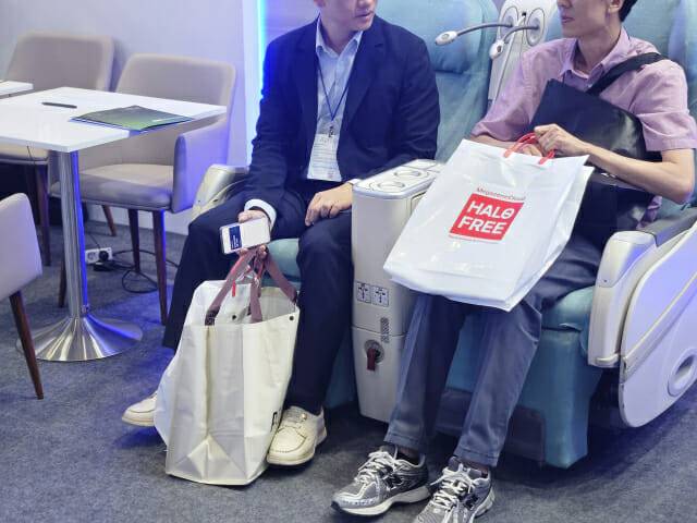 메가존클라우드 부스 참관객들이 비행기 비즈니스석처럼 꾸며진 공간에서 '헤일로' 가방을 든 채 휴식을 취하는 모습 (사진=지디넷코리아)