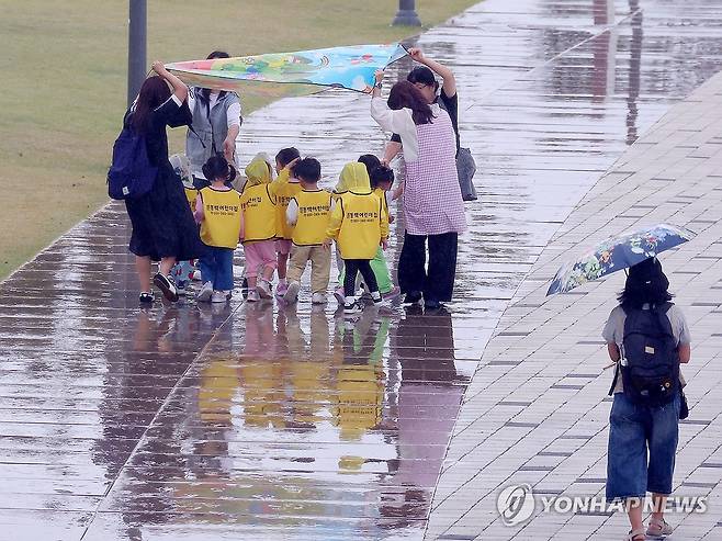 부산 동구 북항친수공원에서 갑자기 비가 내리자 보육교사들이 돗자리를 펼쳐 원생들이 비를 맞지 않도록 막아 주고 있다. [연합뉴스 자료사진]