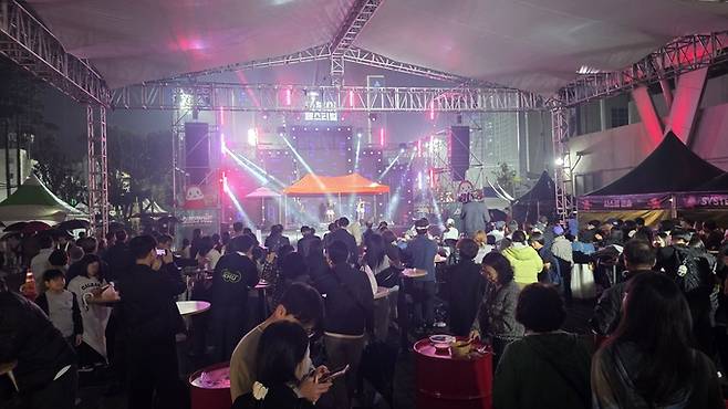 ▲ 24일 궂은비에도 공연장 앞은 관람객들로 북적였다. 우산 아래 떡볶이를 즐기는 시민들 사이로 무대의 음악과 환호가 이어졌다. 김민규 기자