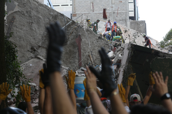 19일(현지시간)규모 7.1 강진이 덮친 멕시코 수도 멕시코시티에서 구급대원들이 구조작업을 벌이고 있다. 건물이 붕괴된 현장 앞에서 생존자의 소리를 듣기 위해 손을 들어올려 침묵을 요청하고 있다. 멕시코시티|AP연합뉴스