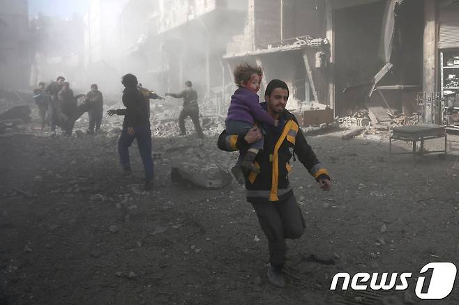 19일(현지시간) 시리아 동구타 지역에서 한 남성이 시리아 정부군의 공습으로 다친 아기를 안고 뛰고 있다. © AFP=뉴스1