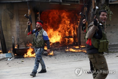 시리아 북서부 아프린에서 불타는 상점 옆을 지나는 터키 연계 반군 [AFP=연합뉴스]