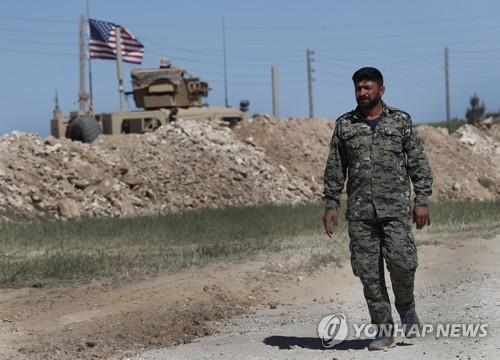 시리아 북부 만비즈에 배치된 미군 차량 주변을 지나는 만비즈 군사위원회 부대원 [AP=연합뉴스]
