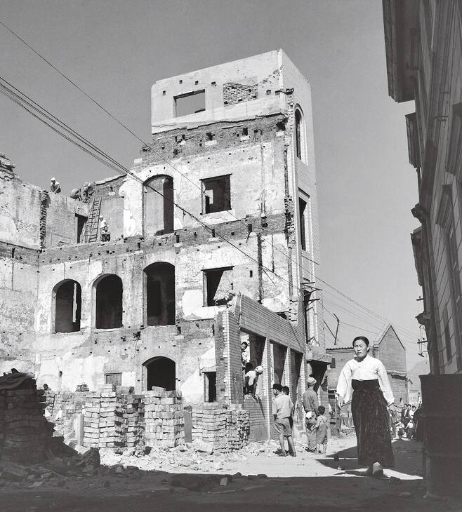 1954년 한국전쟁으로 파괴된 서울 명동에서 복구 작업하는 인부들과 건물 옆을 지나는 여인. 국방부 정훈국 임인식 사진대장이 찍은 것이다. 임정의 제공
