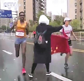 18일 중국 쑤저우에서 열린 마라톤 대회에서 에티오피아 선수와 선두 경쟁 중인 중국 허인리(오른쪽) 선수에게 한 여성 자원봉사자(가운데)가 중국 국기인 오성홍기를 건네 주려 하고 있다. /CCTV