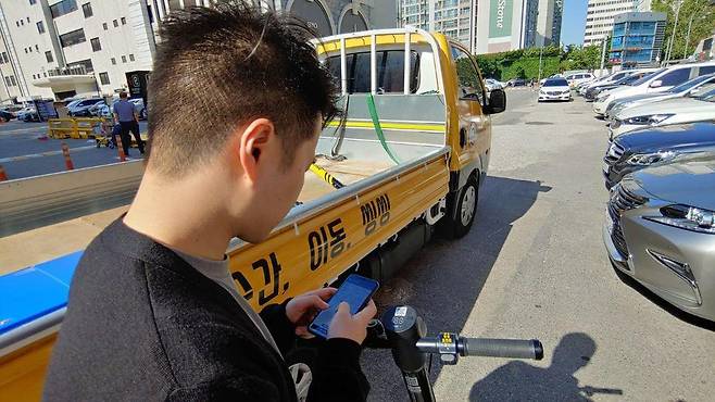 지난 21일 서울 강남의 한 상가건물 앞에서 전동킥보드 공유서비스 ‘씽씽’ 관계자가 휴대전화로 전동킥보드의 위치를 찾고 있다. 박태우 기자