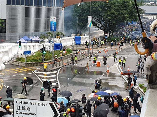 사진 전방에 몰려있는 홍콩 시위대가 입법회(우리의 국회) 앞에서 경찰이 쏜 최루탄과 물대포에도 아랑곳하지 않고 대열을 유지하며 맞서고 있다. 이를 뒤에서 지켜보는 시민들 앞 도로가 물대포 흔적으로 흥건하다. 김광수 특파원