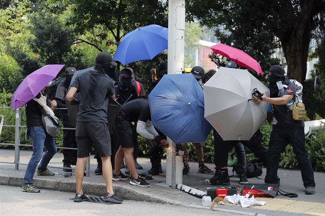 지난달 24일 홍콩 시내에서 우산으로 몸을 가린 시위대 한 무리가 길가에 설치된 스마트 가로등을 쇠톱으로 자르고 있다. 홍콩=AP 연합뉴스