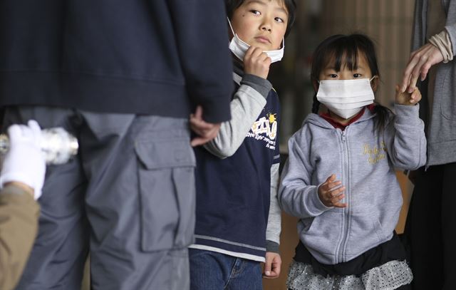 2011년 동일본 대지진으로 후쿠시마 원전 폭발 사고가 발생, 최악의 방사선 유출이 우려되는 일본 후쿠시마 청사에서 마스크를 쓴 일본 어린이들이 방사능 오염 검사를 받고 있는 어른들을 물끄러미 바라보고 있다. 후쿠시마=AP연합뉴스