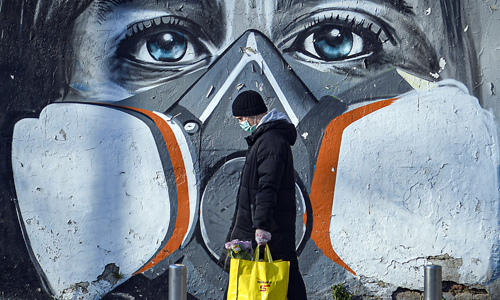 16일(현지시간) 이탈리아 밀라노에서 방독면을 쓴 사람을 그린 벽화 옆에서 한 남자가 식료품을 들고 걷고 있다. 밀라노=EPA연합뉴스
