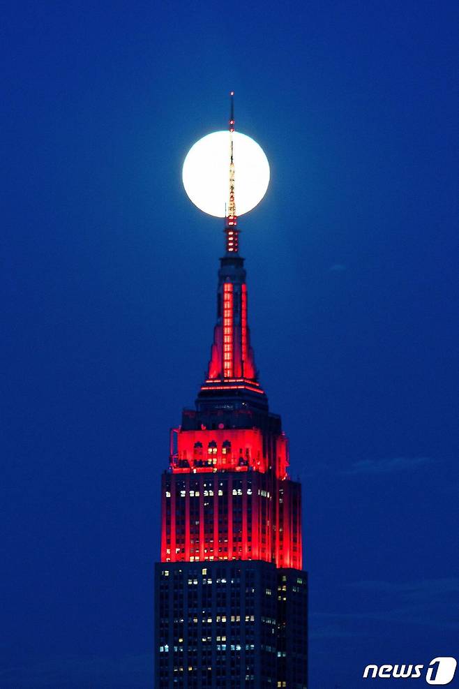 7일(현지시간) 코로나19 환자들과 연대의 의미로 붉은 조명을 밝힌 뉴욕 맨해튼가에 있는 엠파이어 스테이트 빌딩 위로 슈퍼문이 떠오르고 있다. © 로이터=뉴스1 © News1 우동명 기자