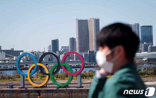 지난달 25일 일본 도쿄 오다이바의 올림픽 오륜 조형물 앞을 마스크를 쓴 한 시민이 지나가고 있다. © AFP=뉴스1