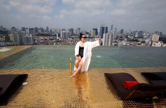 한 여성이 2일(현지시간) 베트남 하노이에 새로 문을 연 ‘돌체 하노이 골든 레이크 호텔’의 금으로 도금한 객실 루프탑 인피니티풀에서 기념촬영을 하고 있다.로이터 연합뉴스