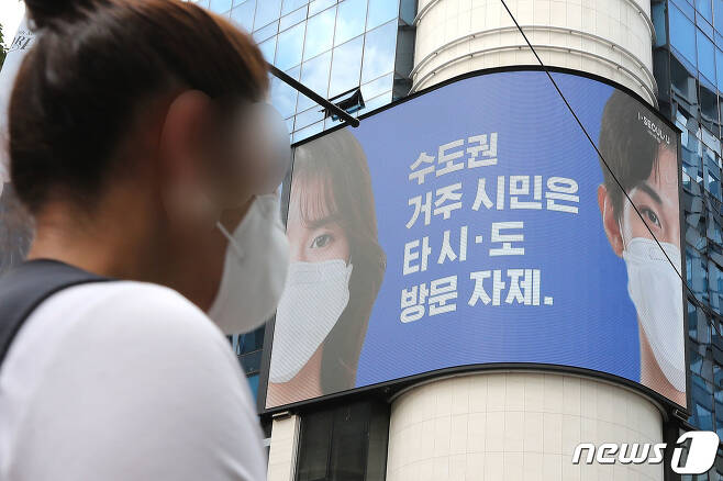 23일 서울 중구 명동거리에서 한 시민이 전광판에 나오는 마스크 쓰기 캠페인 화면 앞을 지나고 있다. 서울특별시는 24일 0시부터 마스크 착용을 의무화하기로 했다./뉴스1 © News1 임세영 기자