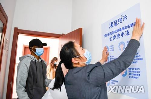 중국의 한 대학 교수가 코로나19 위생 지침에 대한 포스터를 붙이는 모습을 아프리카인 유학생이 지켜보고 있다.[신화=연합뉴스 자료사진]