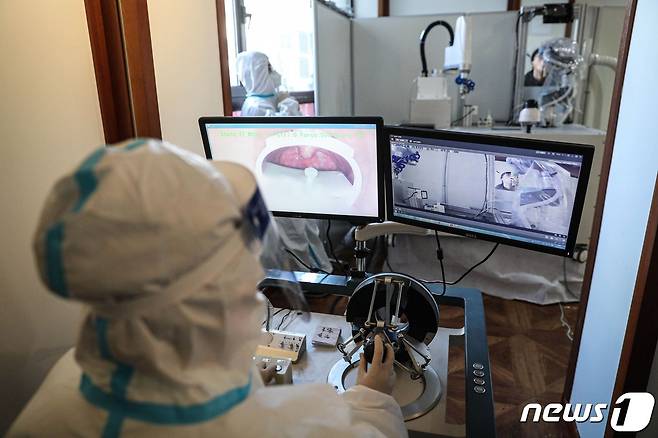 13일 중국 랴오닝성 선양시에서 의료진이 모니터를 보며 코로나19 진단검사용 검체 채취용 로봇을 조종하고 있다. © AFP=뉴스1