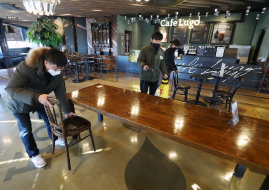 On the afternoon of January 17, one day before people are allowed to eat and drink inside cafes, employees at a café in Dalseo-gu, Daegu disinfect the café and return the chairs to the tables. Yonhap News