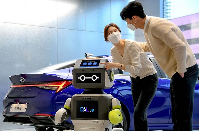 현대차그룹이 25일 공개한 고객 응대 서비스 로봇 ‘DAL-e’(달이)가 고객들과 함께 서 있다. 달이는 이날부터 서울 현대차 송파대로지점에서 한 달간 시범 서비스에 들어갔다.  현대차그룹 제공