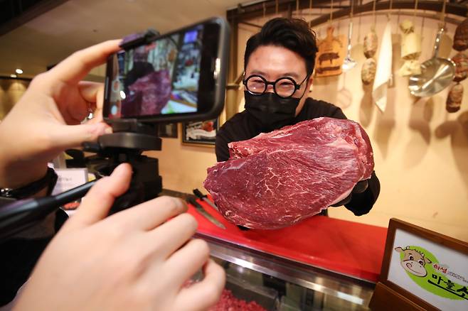 A butcher at the Lotte Department Store in Daegu displays meat during a live commerce show while chatting to viewers on Dec. 29, 2020. (Yonhap)