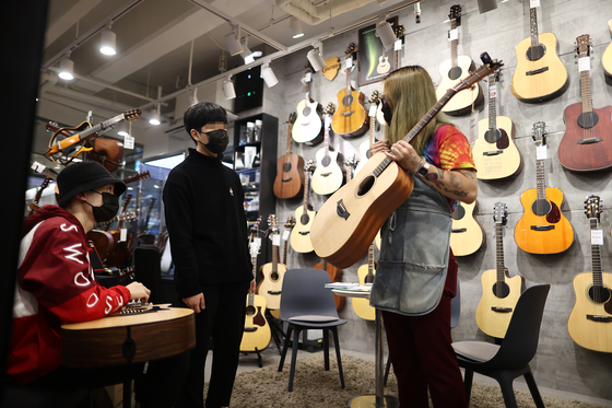 A store clerk shows a guitar to customers at an instrument shop in Seoul on Tuesday. According to Gmarket, an online market run by eBay Korea, guitar sales rose 44 percent between Dec. 25 and Jan. 24 as more people have been staying home due to the strict social distancing due to Covid-19. [YONHAP]