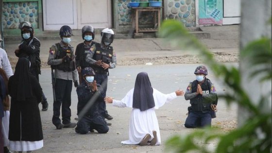 안 로사 누 따웅 수녀가 8일(현지시간) 미얀마 북부 카친주 미치나시에서 시위대를 진압하러 온 경찰들 앞에 무릎을 꿇고 '발포를 자제해 달라'고 호소하고 있다. 경찰 두 명도 함께 무릎을 꿇고 손을 모았다. [SNS 캡처]