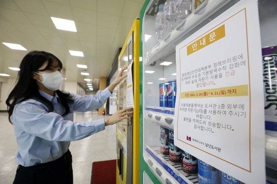 신종 코로나바이러스 감염증(코로나19) 신규 환자가 551명 늘어 500명대 중반까지 치솟은 가운데 부산도 수도권처럼 사회적 거리두기 2단계를 적용하기로 했다. 29일 오후 서울 용산구 남산도서관에서 한 직원이 음료자판기에 사용금지 안내문을 붙이고 있다.뉴스1