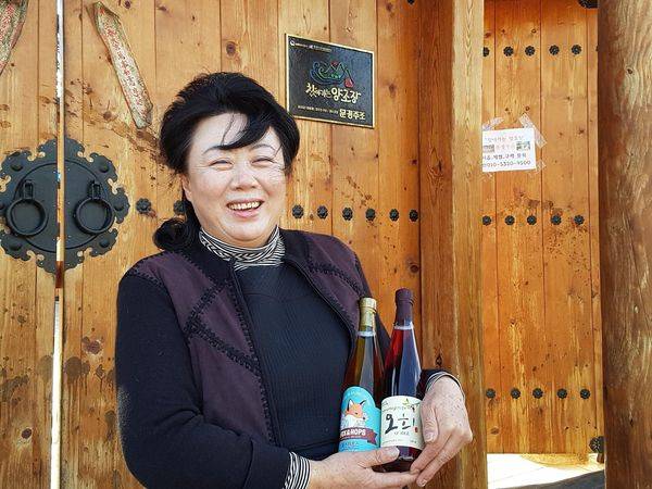 문경주조 홍승희 대표가 폭스앤홉스, 오희를 들고 양조장 입구에서 웃고 있다. 문경주조는 찾아가는 양조장으로도 선정돼 일반인들이 술빚기 같은 체험을 할 수 있다.